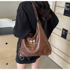 Detail of caramel brown tote bag featuring silver bow accent and chain shoulder strap