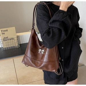 Detailed view of brown leather bucket bag with silver bow accent and chain trim