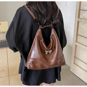 Close-up of vintage brown leather bucket bag with metal bow buckle and chain strap