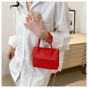Close-up of red lychee grain leather mini bag with gold chain strap on white shirt