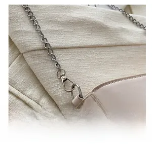 Detail of silver chain lobster clasp and textured beige leather on crossbody bag