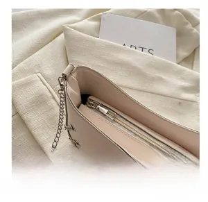 Close-up of smooth silver zipper and chain strap on a minimalist beige baguette bag