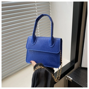 Détail du sac à main bleu royal avec motif litchi, chaîne dorée et poignée élégante