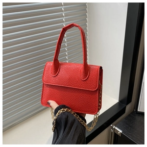 Détail du mini sac rouge en cuir grainé avec chaîne dorée sur le rebord d'une fenêtre
