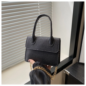 Détail d'un sac à main noir en cuir texturé avec une élégante bandoulière en chaîne dorée