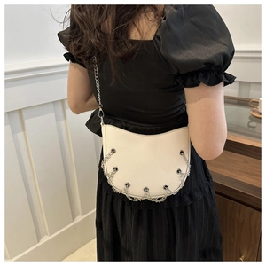 Detailed view of white half-moon shoulder bag with metal eyelets and silver chain fringe