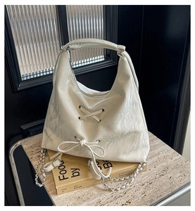 Detail of white glossy hobo bag with lace-up bow design and silver chain strap