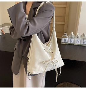 Detail of cream hobo bag featuring lace-up bow design and silver chain strap details