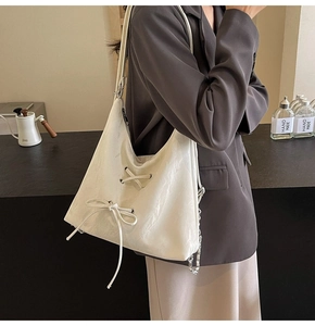 Detail of cream hobo bag featuring lace-up bow design and silver chain strap