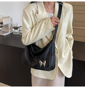 Détail de la boucle papillon en métal liquide argenté sur un sac en similicuir noir
