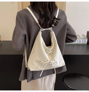 Detail of white triangular backpack with bow ribbons and crisscross lacing detail