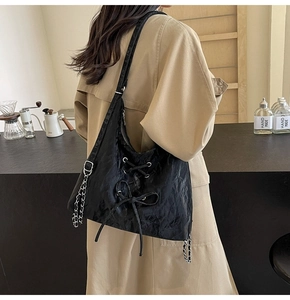 Detail of black pleated bag with crisscross drawstring and silver chain on model