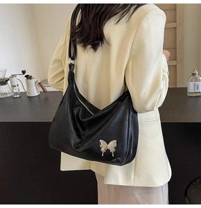 Détail d'un sac à épaule en similicuir noir avec un pendentif papillon sur un mannequin