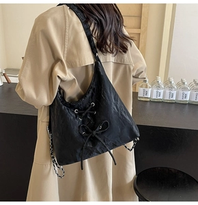 Detail of a black pleated shoulder bag with lace-up bow and silver chain strap