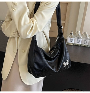 Détail d'un grand sac hobo en cuir PU noir texturé avec papillon argenté élégant