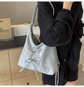 Close-up of silver-gray metallic wrinkled texture bag with bow and chain detail