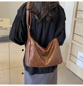 Detail of a brown leather hobo shoulder bag featuring patchwork stitching and a wide strap