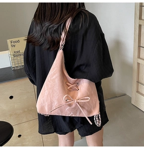 Close-up of pink pleated shoulder bag with ribbon ties and metal chain detail