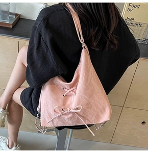 Detailed side view of pink hobo bag with ribbon bows and silver chain strap on a shoulder