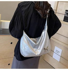 Détail du sac à bandoulière argenté avec décoration papillon doré et texture souple