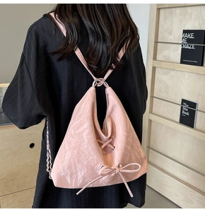 Detail of pink triangular backpack featuring drawstring bow and metal chain straps