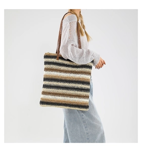Dettaglio della borsa tote intrecciata a righe colorate con manici in pelle marrone indossata