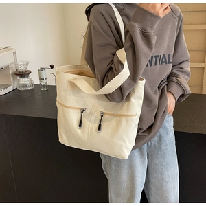 Detail of cream canvas tote bag with dual vertical zipper pockets and woven rope pulls