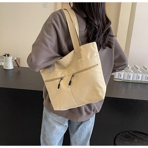 Detail of cream canvas tote bag with functional diagonal zipper pockets and wide straps
