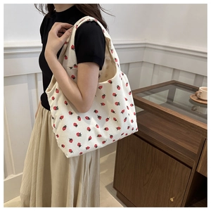 Detail of off-white corduroy tote bag featuring strawberry patterns and wide shoulder strap