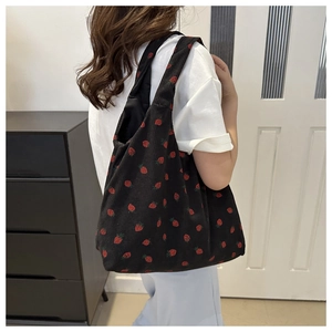 Detail of black corduroy tote bag with red strawberry pattern shown on shoulder