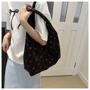 Detail view of black corduroy tote bag with strawberry prints worn over shoulder