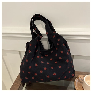 Close-up of black corduroy tote bag featuring red strawberry embroidery and soft texture