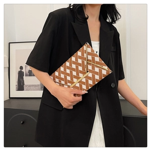 Chic brown and white geometric envelope clutch bag with gold trim held by a model