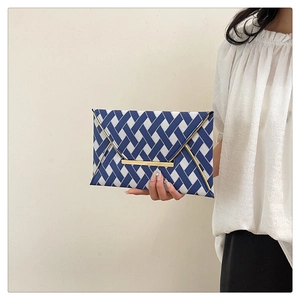 Detail of blue and white woven envelope clutch featuring elegant gold metal edge trim