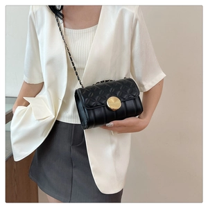 Close-up of black quilted leather shoulder bag with golden round metal lock and chain strap