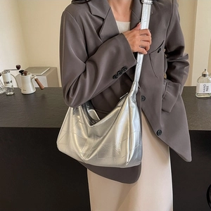 Metallic silver crescent shoulder bag with stitched texture on a female model
