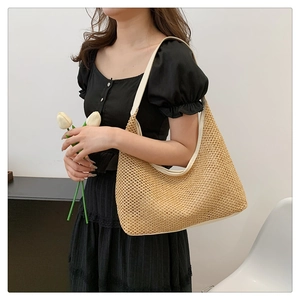 Handwoven straw shoulder bag with white leather straps in a minimalist indoor setting