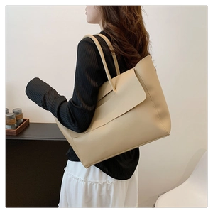 Side view of a large beige minimalist tote bag carried by a model for size perspective