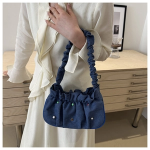 Detail of denim shoulder bag with colorful beads and pleated handle on a wooden cabinet