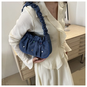 Detail of blue denim shoulder bag featuring colorful rivets and pleated fabric textures