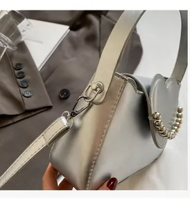 Detail of silver heart-shaped crossbody bag with metallic bead handle and leather texture