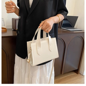 Détail d'un sac à main blanc structuré avec boucle dorée porté par un mannequin en costume