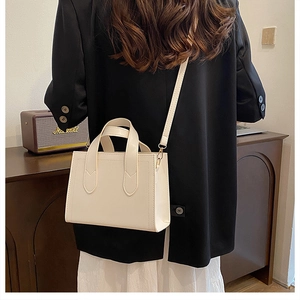 Sac à main structuré blanc crème minimaliste porté avec un blazer noir en extérieur