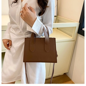 Détail d'un sac cabas structuré en cuir marron foncé tenu par un mannequin au style épuré