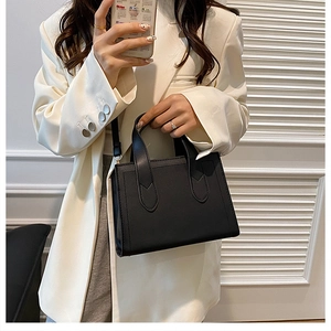 Détail d'un sac à main noir en cuir structuré avec bandoulière sur un costume blanc élégant