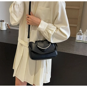 Fashionable black crossbody bag with heart-shaped pearl flap shown on a model