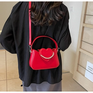 Detail of red heart-shaped bag with white pearl chain and glossy PU leather finish