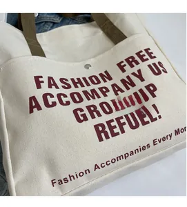 Detail of off-white canvas tote bag featuring maroon letters and brown woven shoulder strap