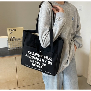 Detail of black canvas tote bag with front pocket and white fashion lettering print