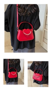 Detail view of red heart-shaped shoulder bag with pearl accents worn by a model